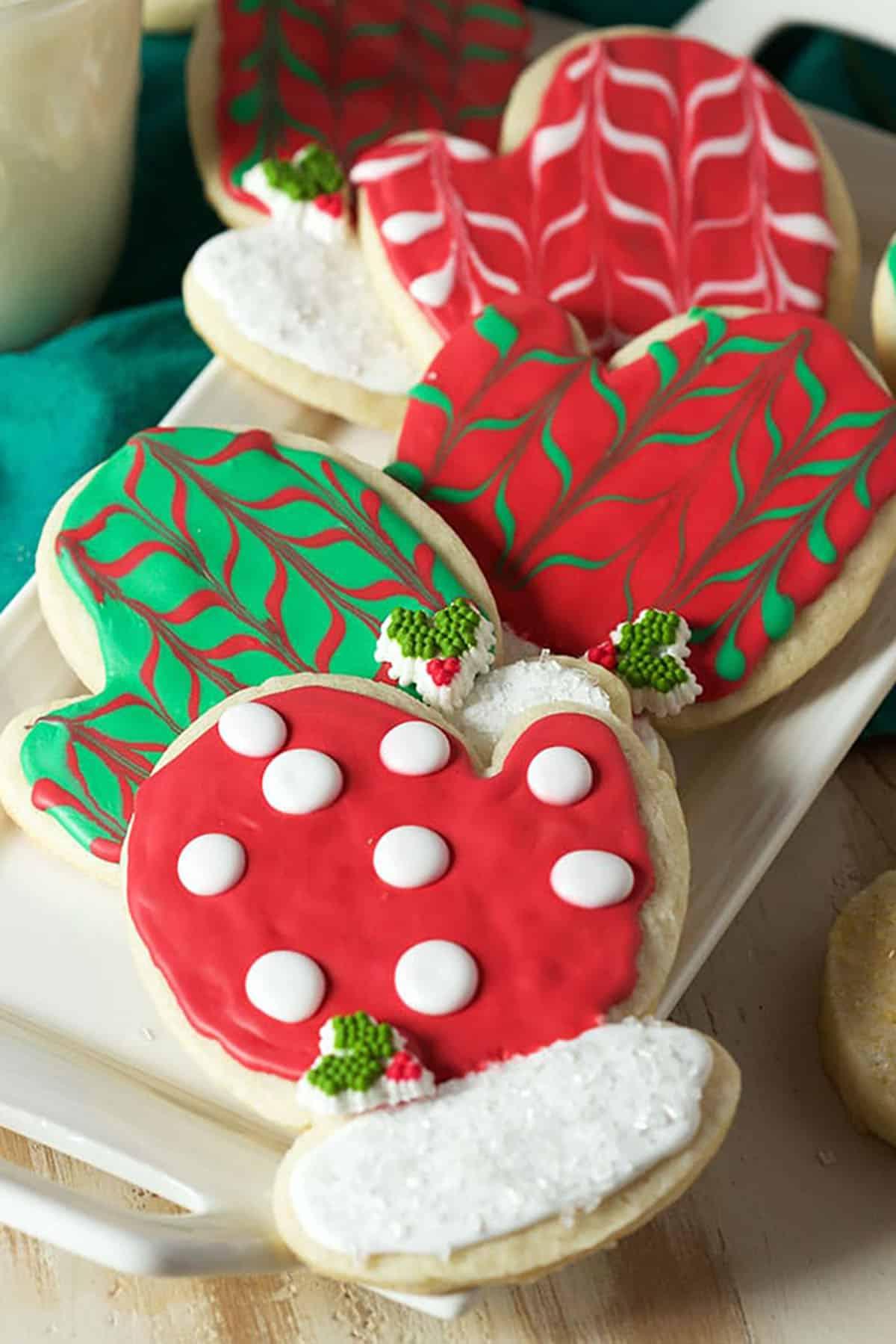 Biscotti di Natale allo zucchero 2 Biscotti di zucchero a forma di guanto decorati con glassa reale rossa e verde, adagiati su un piatto bianco immacolato.