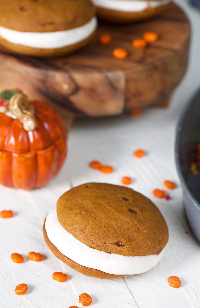 **Whoopie Pies alla Zucca con Ripieno al Mascarpone d'Acero** 2 Whoopie pie alla zucca su sfondo bianco con spolverata di decorazioni a forma di zucca.