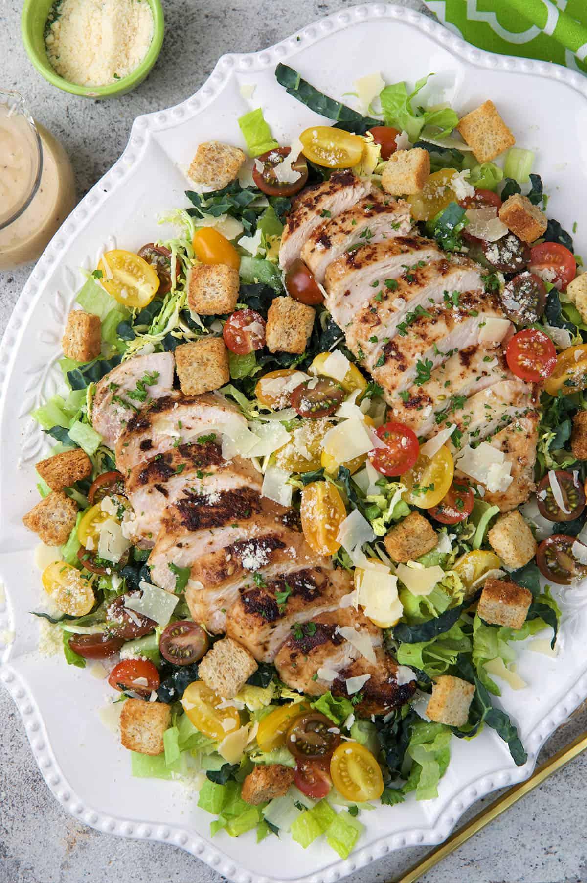 Insalata Caesar con Pollo 2 Un grande piatto da portata bianco è sormontato da insalata Caesar con pollo.