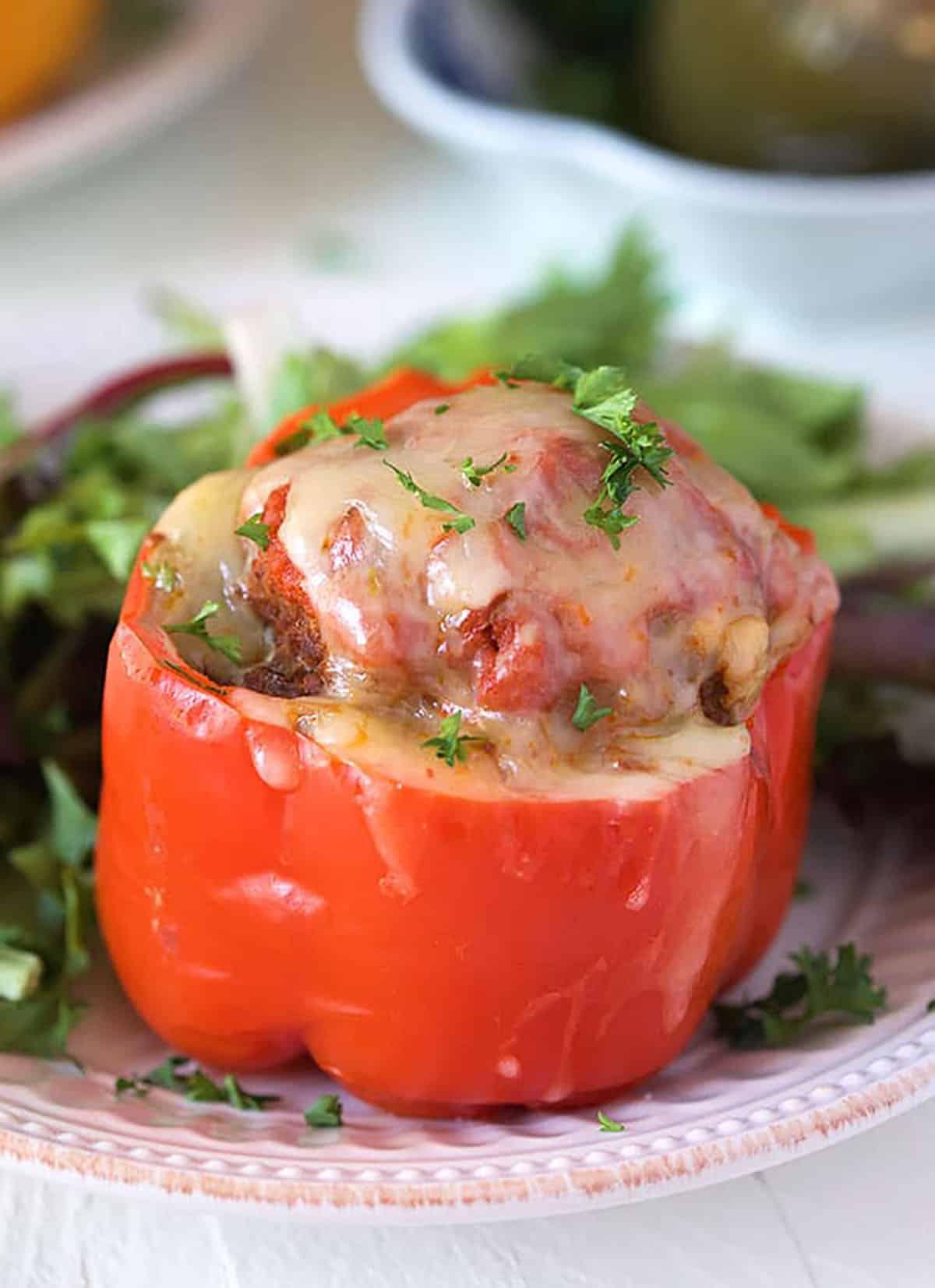 Ricetta Peperoni Ripieni Instant Pot 2 Peperone rosso ripieno, ricoperto di formaggio, su un piatto bianco con verdure.