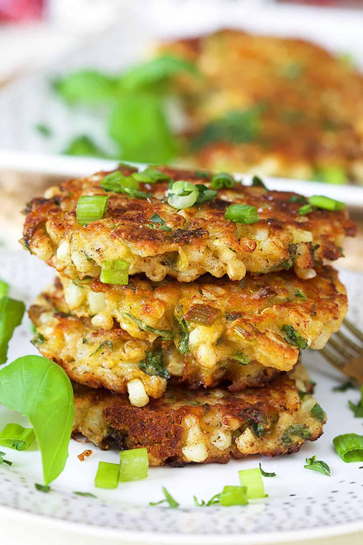 Frittelle di Mais all'Antica con Cheddar e Basilico 2 Tre frittelle di mais impilate su un piatto bianco con un rametto di basilico.