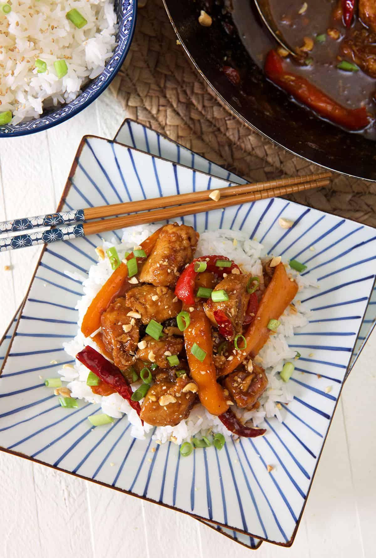 Pollo Kung Pao Facile 2 Un piatto di pollo Kung Pao servito con riso bianco su un piatto a strisce.