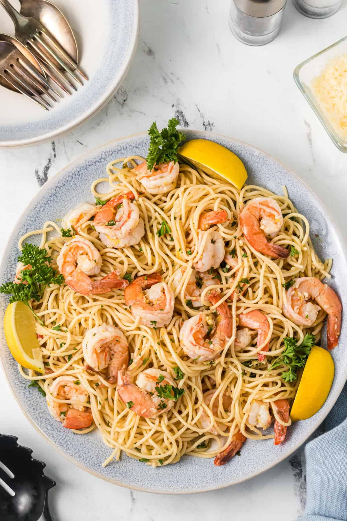 Gamberi Scampi 2 Un grande piatto bianco è presentato con noodles, gamberi e fette di limone.