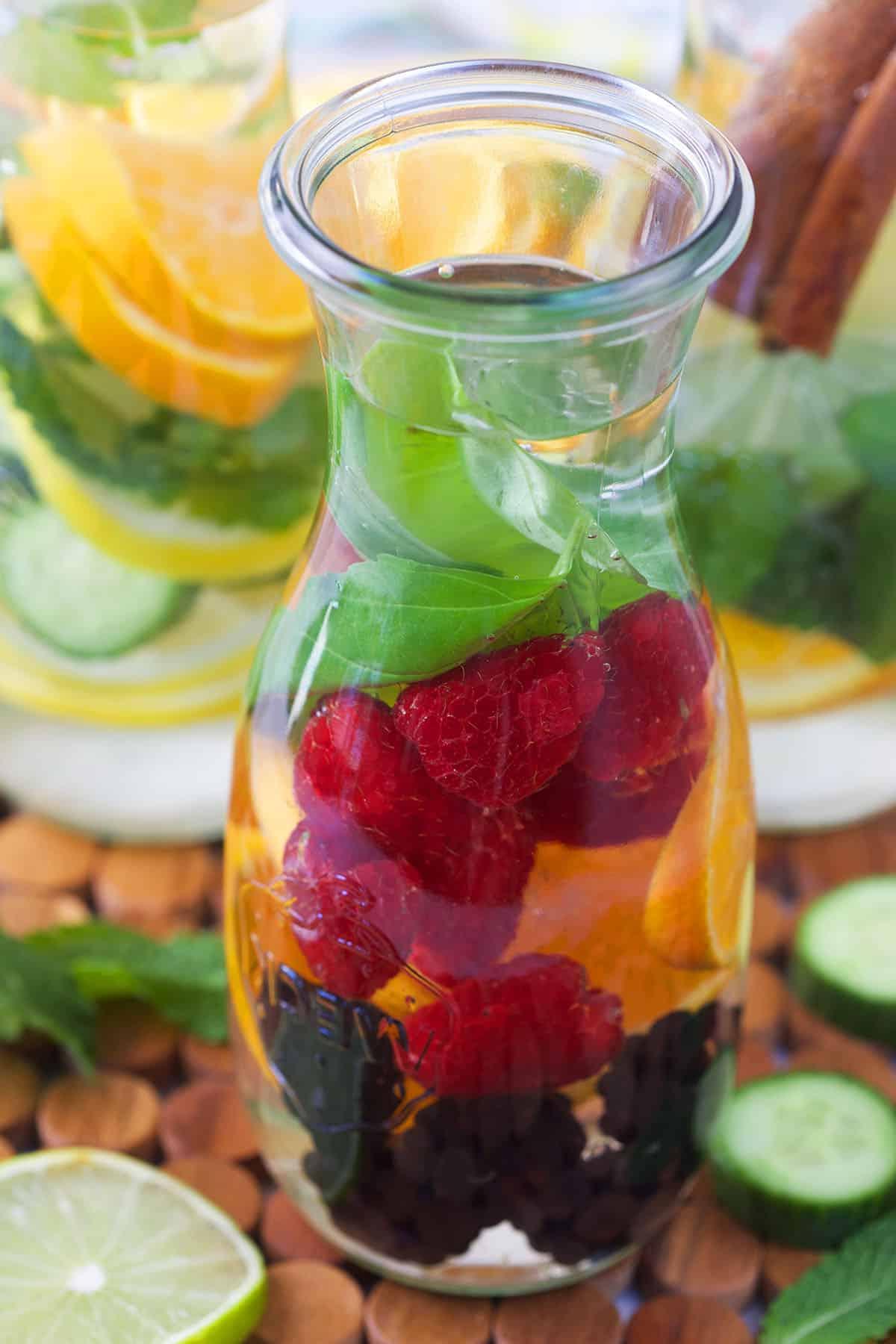 Acqua Infusa di Frutta 2 Una bottiglia di vetro di acqua aromatizzata con frutti di bosco, basilico e arance.