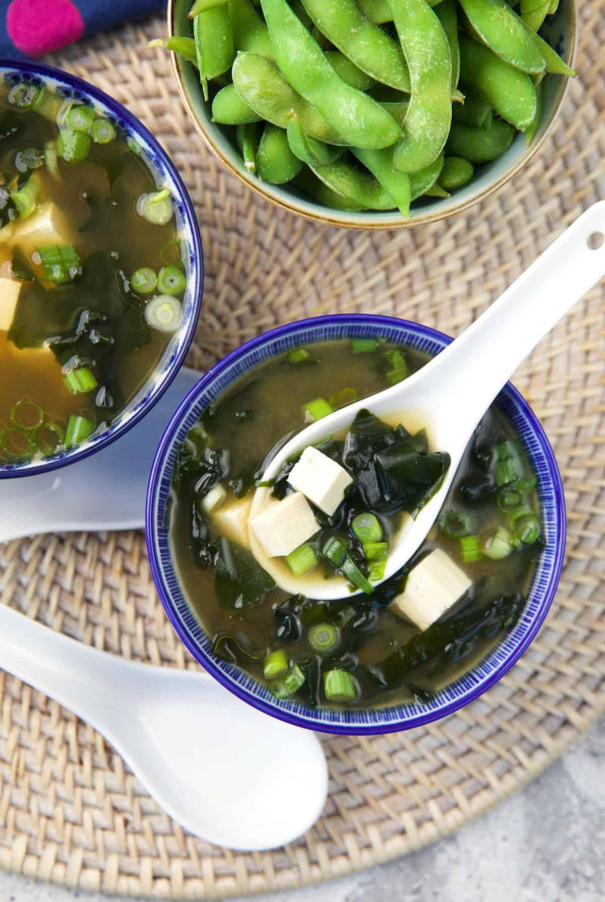 Zuppa di Miso Veloce e Facile 2 Un cucchiaio bianco solleva una porzione di zuppa fumante da una ciotola, mostrando il tofu e le alghe.