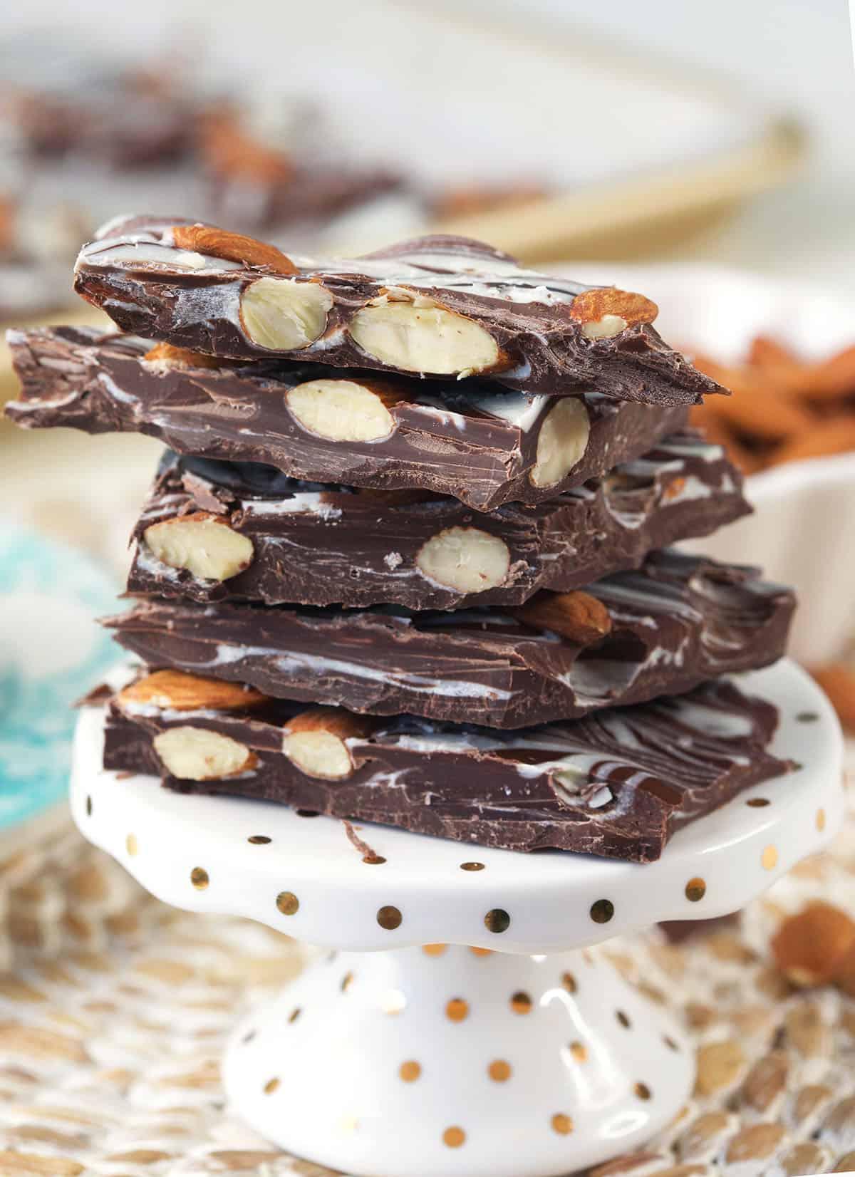 Facile Scorza di Mandorle Fatta in Casa 2 Un mucchio di scorze di mandorle al cioccolato è presentato su un piccolo alzata per dolci.