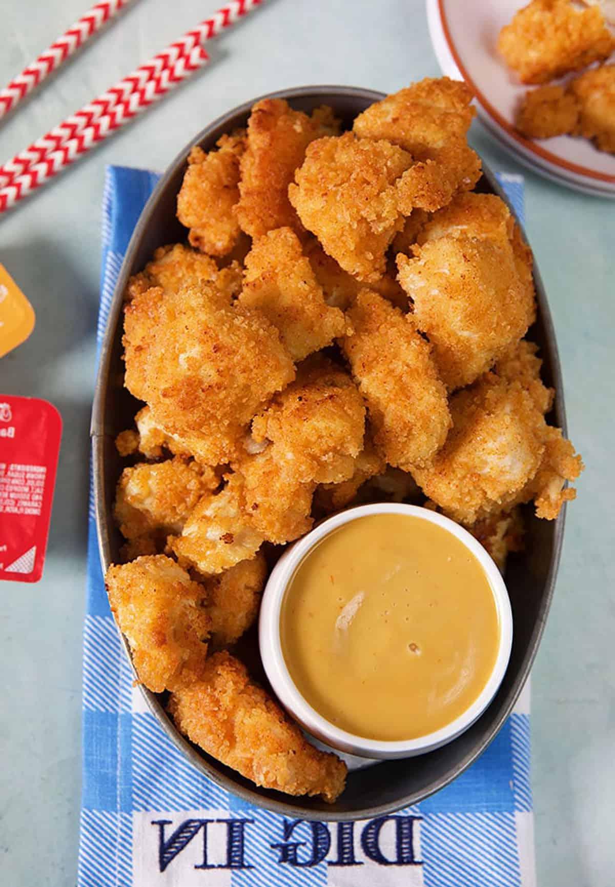 **Nuggets Imitazione Chick-fil-A** 2 Nuggets di pollo Chick-Fil-A in una teglia di metallo con salsa su un tovagliolo a quadri blu e bianco.
