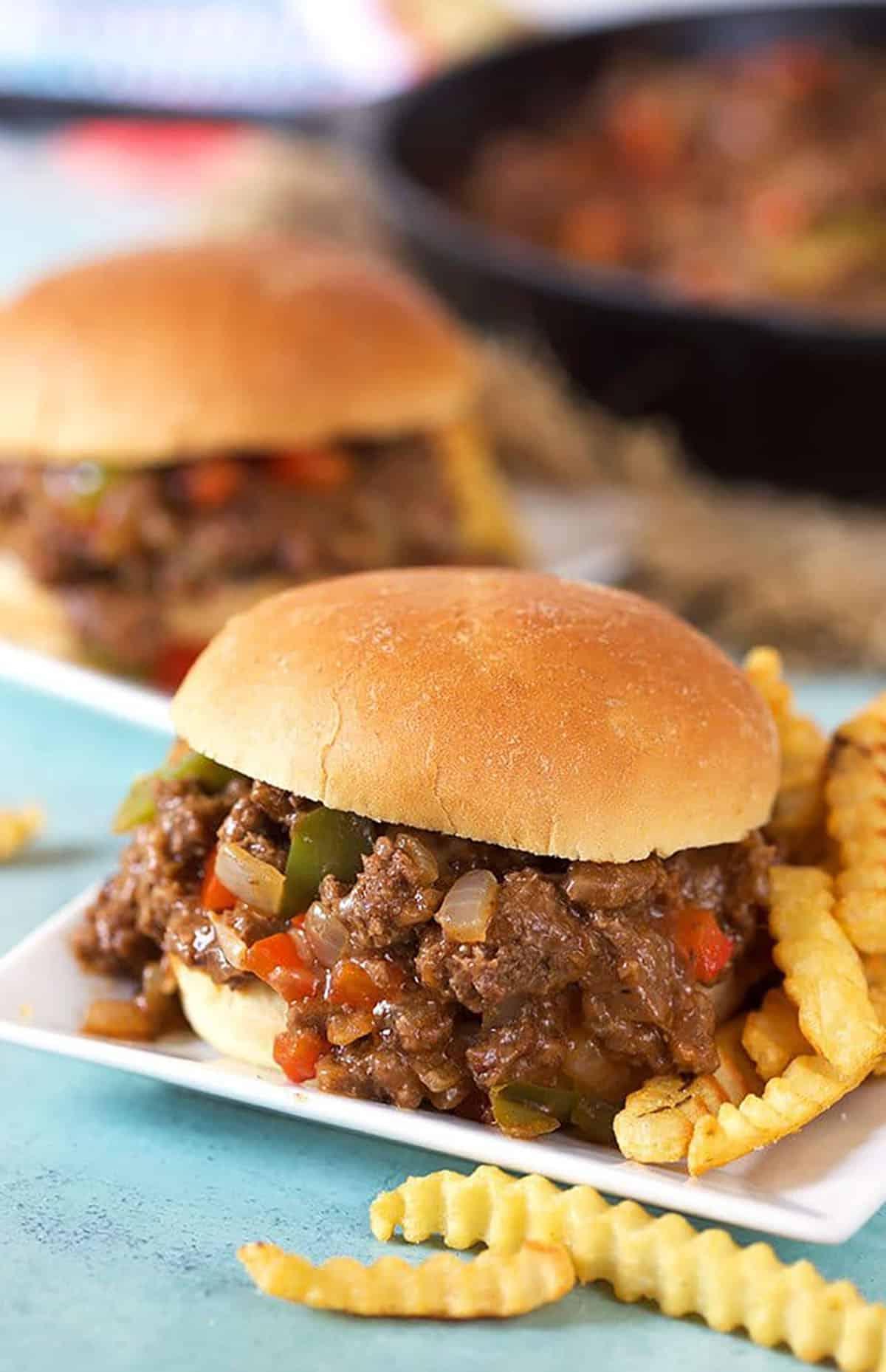 Sloppy Joe al Philly Cheesesteak 2 Philly Cheesesteak Sloppy Joe su un piatto quadrato bianco con patatine fritte a taglio ondulato.