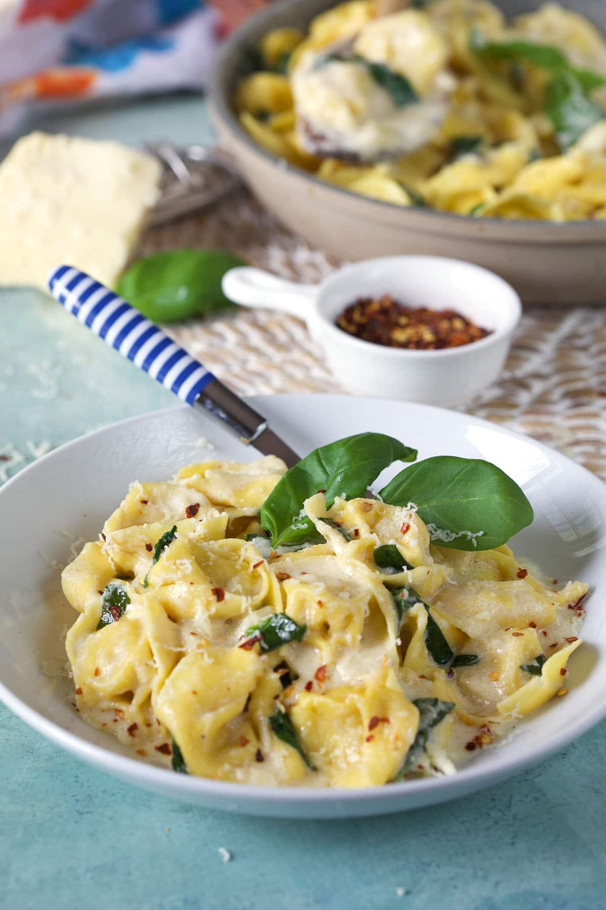 Tortellini all'Asiago 2 Una ciotola bianca contiene una porzione abbondante di tortellini all'Asiago, fumanti e cremosi.