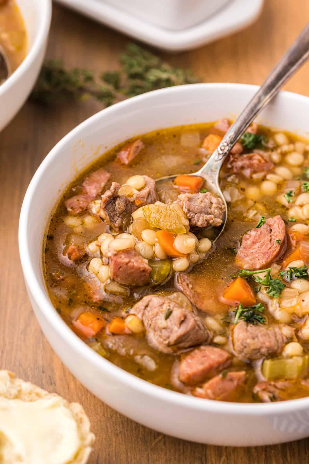 Zuppa di Manzo e Orzo con Salsiccia Andouille 2 Un cucchiaio sta immergendo in una ciotola piena di zuppa.