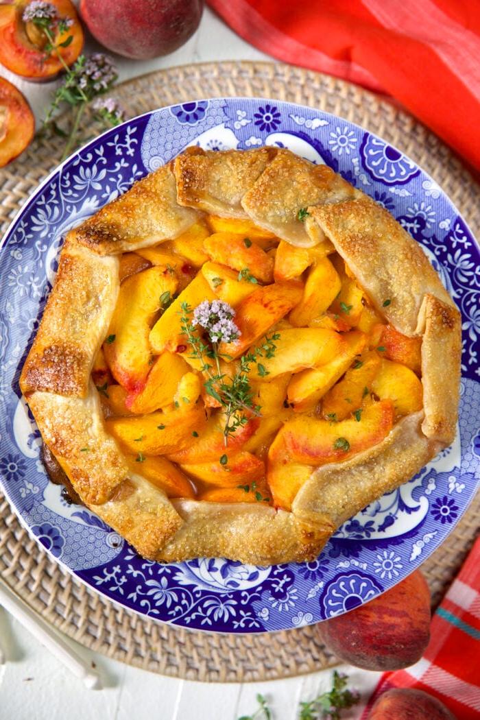 Galette di Pesche al Miele e Timo 2 Una galette di pesche al miele e timo è presentata su un piatto blu e bianco.