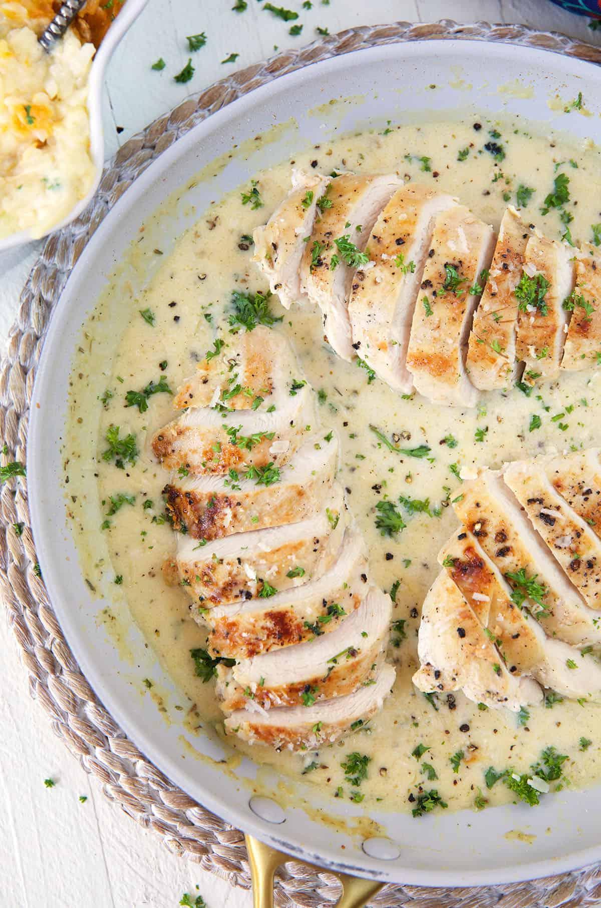 **Petto di Pollo Scottato in Padella con Salsa al Parmigiano e Aglio** 2 Diversi petti di pollo affettati sono ricoperti di salsa bianca in una padella.