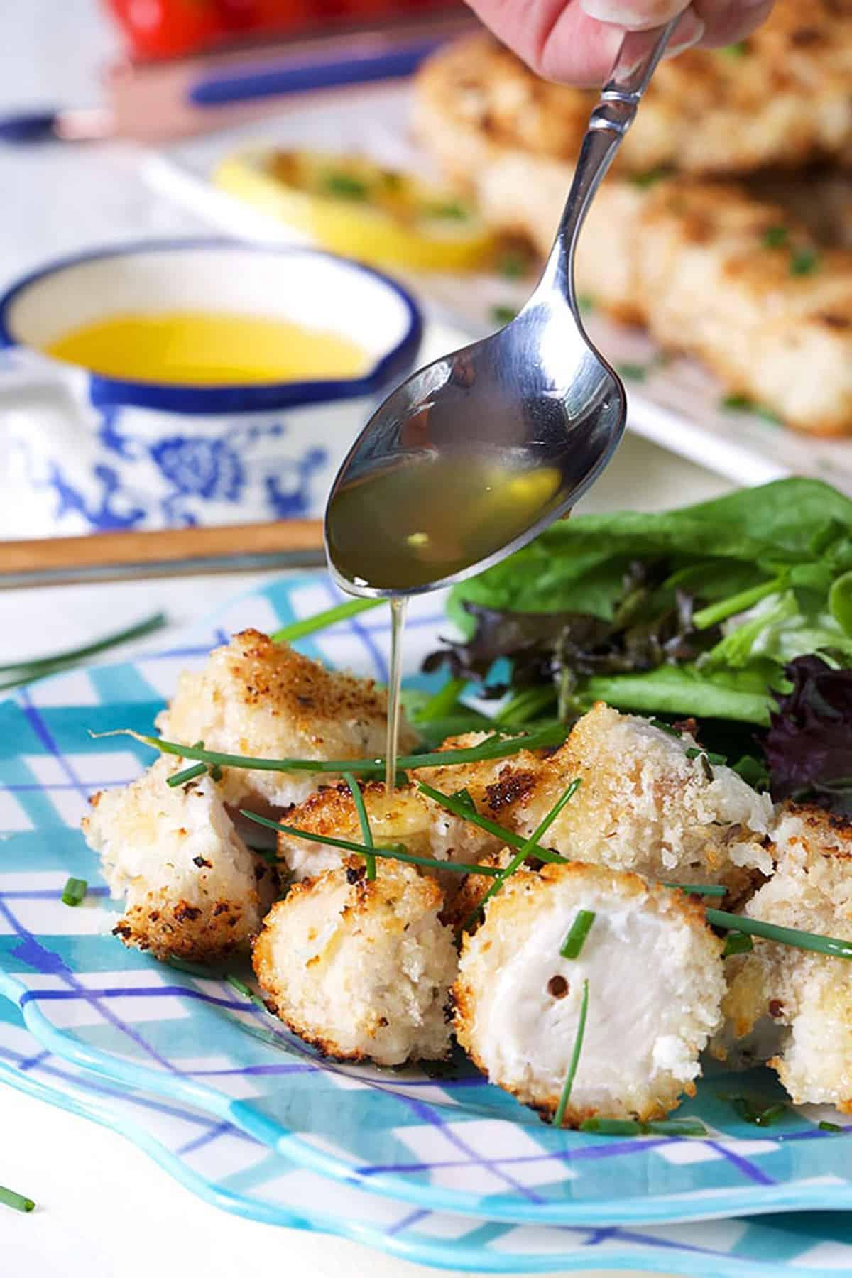 Spiedini di Pollo alla Griglia 3 Spiedini di pollo su un piatto a quadri blu e bianco con burro che viene gocciolato sopra con un cucchiaio.