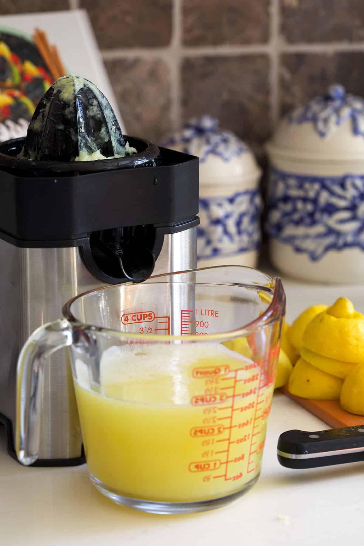 Ricetta della Limonata Fatta in Casa 3 Spremiagrumi elettrico con una caraffa di succo di limone davanti al beccuccio.