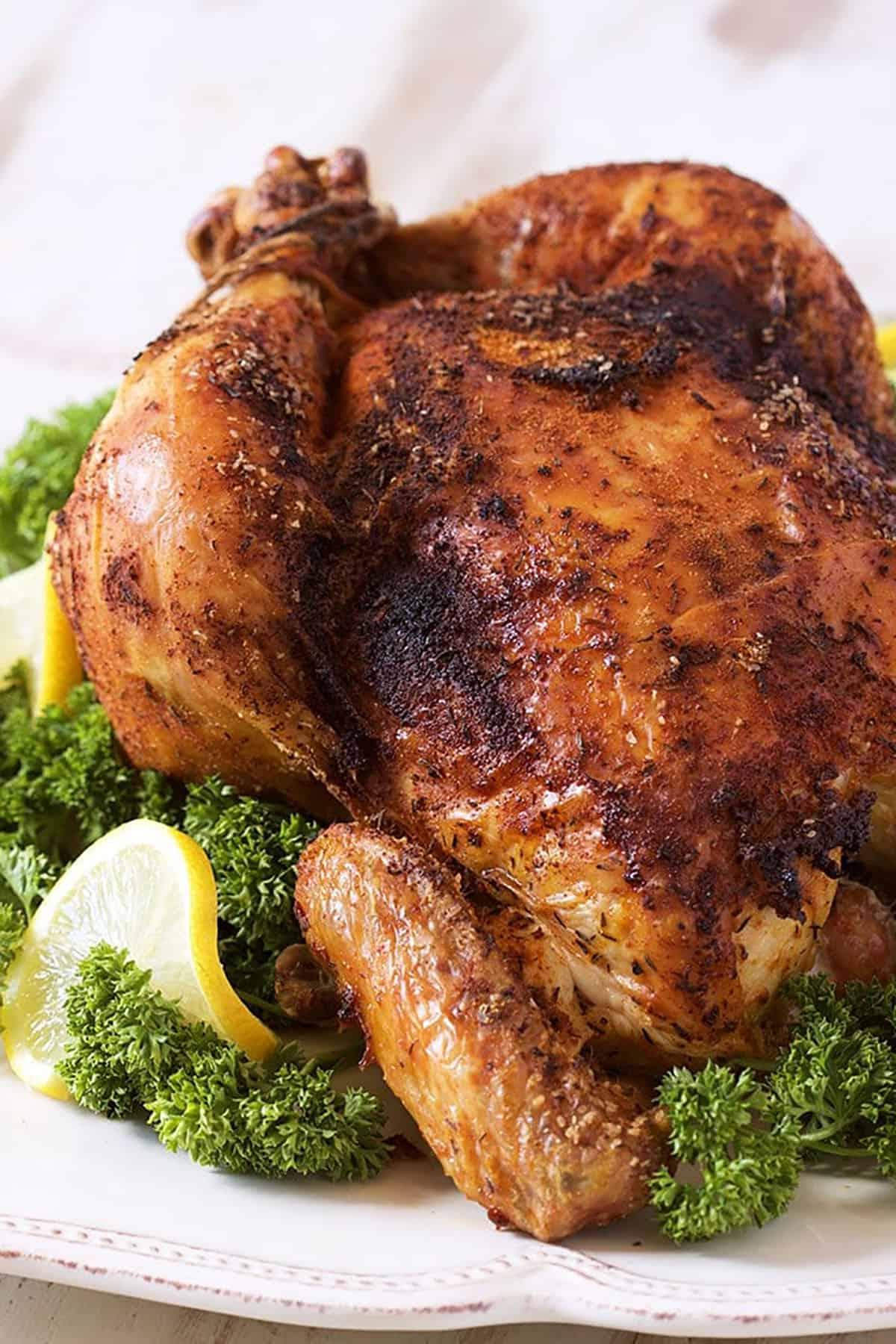 Come preparare il Pollo allo Spiedo 3 Pollo Arrosto su un piatto bianco con prezzemolo e limoni.