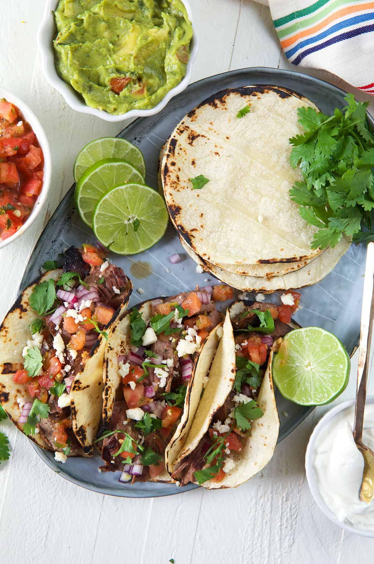 Semplici Tacos di Carne Asada 3 Le tortillas sono posizionate accanto a una porzione di tre tacos di carne asada.