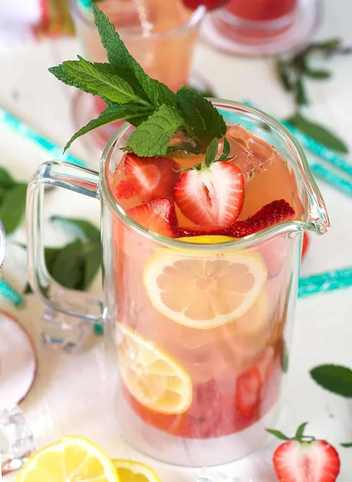 Limonata alle Fragole Fatta in Casa 3 Limonata alla fragola in una brocca trasparente con fragole e limone come guarnizione.