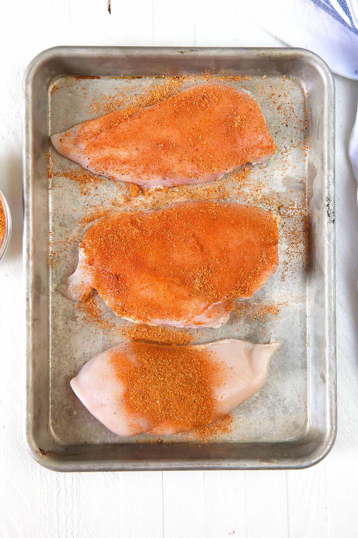 Petti di Pollo alla Griglia 3 Tre petti di pollo sono stati conditi e sono presentati su una teglia.