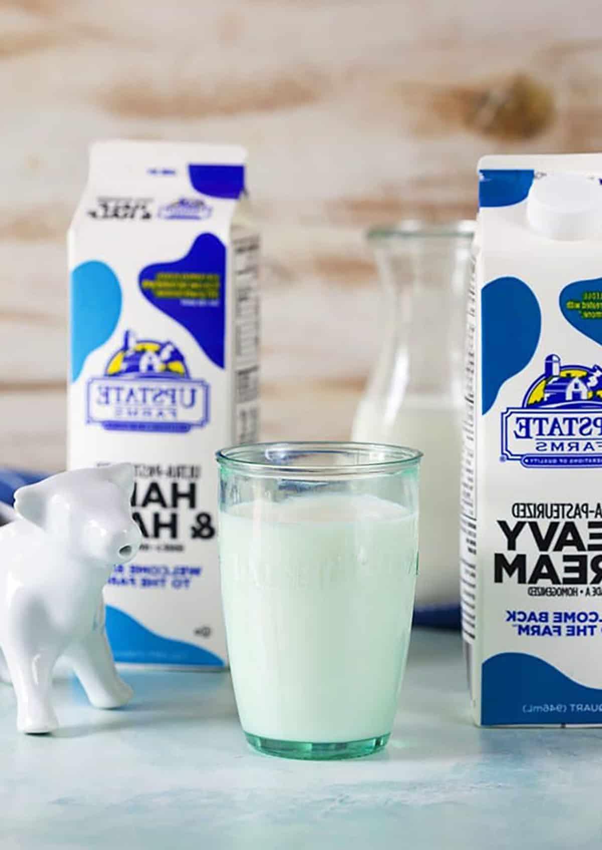 **Cos'è il Latte e Panna (e come prepararlo da zero!)** 3 Cartone di panna, bicchiere di latte e un cartone di half and half con una lattiera a forma di mucca bianca.