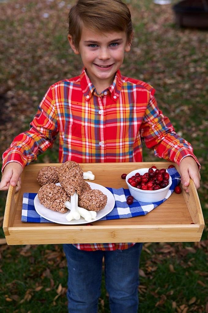 Cosce di tacchino di riso soffiato 3 Ragazzo che tiene un vassoio con cosce di tacchino di Rice Krispies e mirtilli rossi.