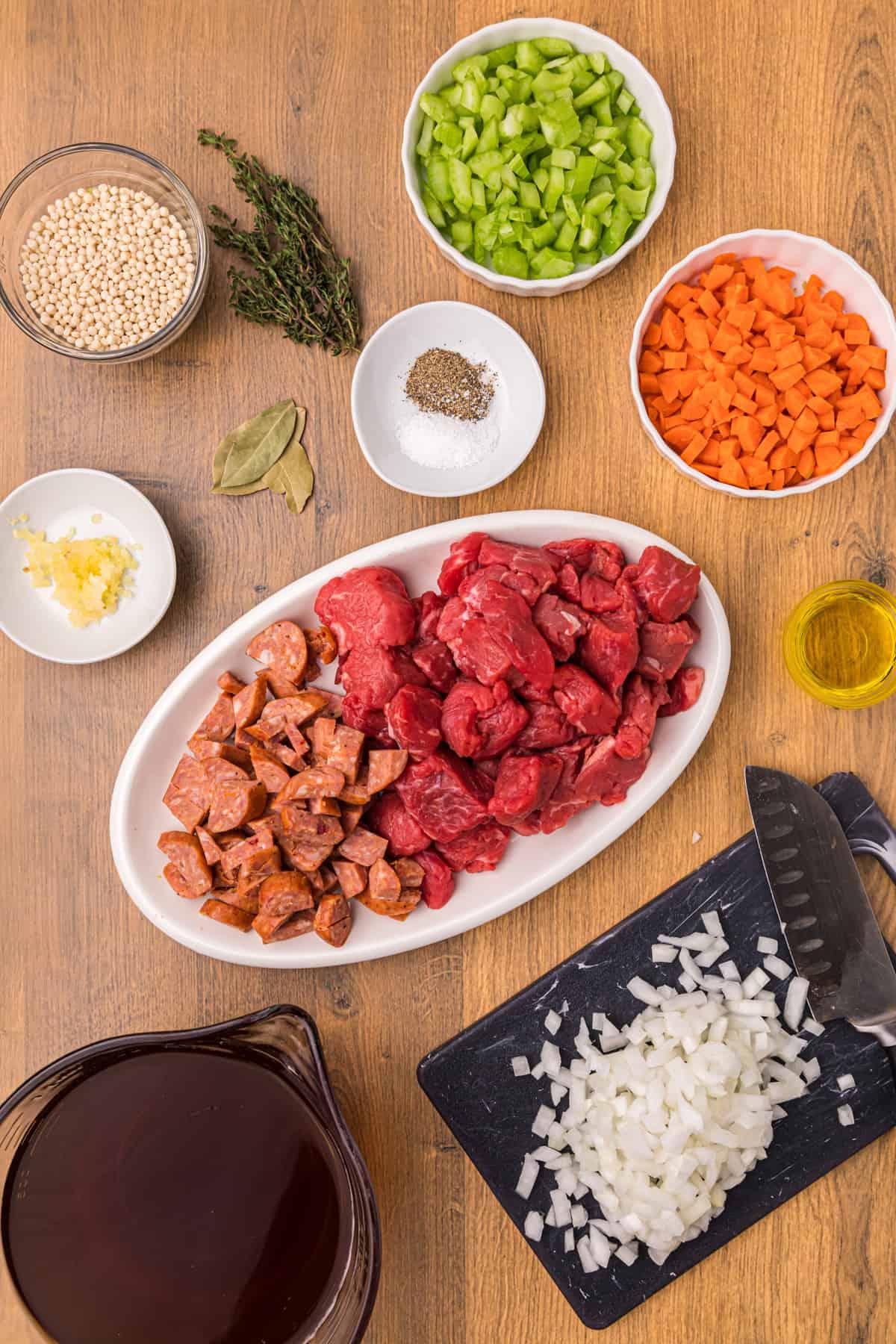 Zuppa di Manzo e Orzo con Salsiccia Andouille 3 Gli ingredienti per la zuppa di manzo e orzo sono posizionati su una superficie marrone.
