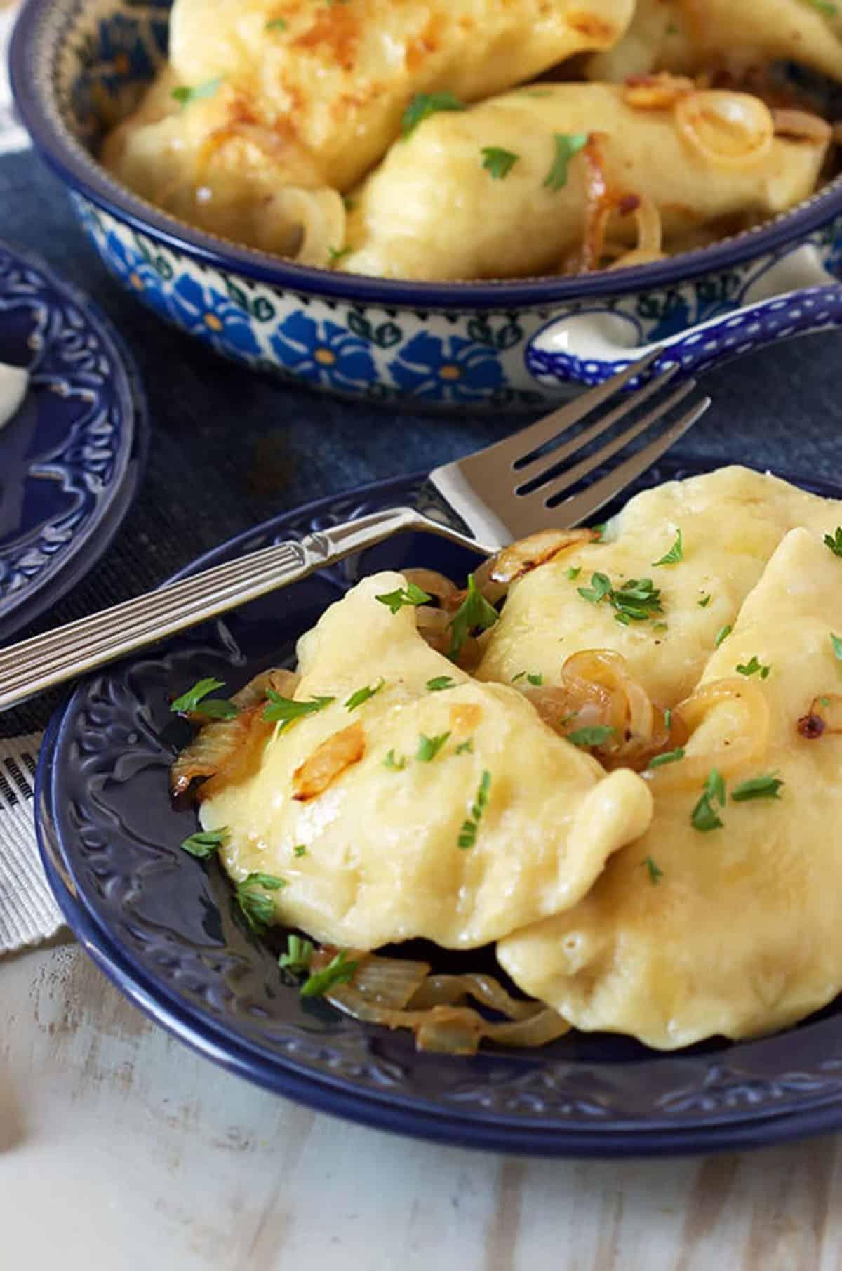 La migliore ricetta di pierogi di patate 3 Pierogi polacchi di patate su un piatto blu con una forchetta.