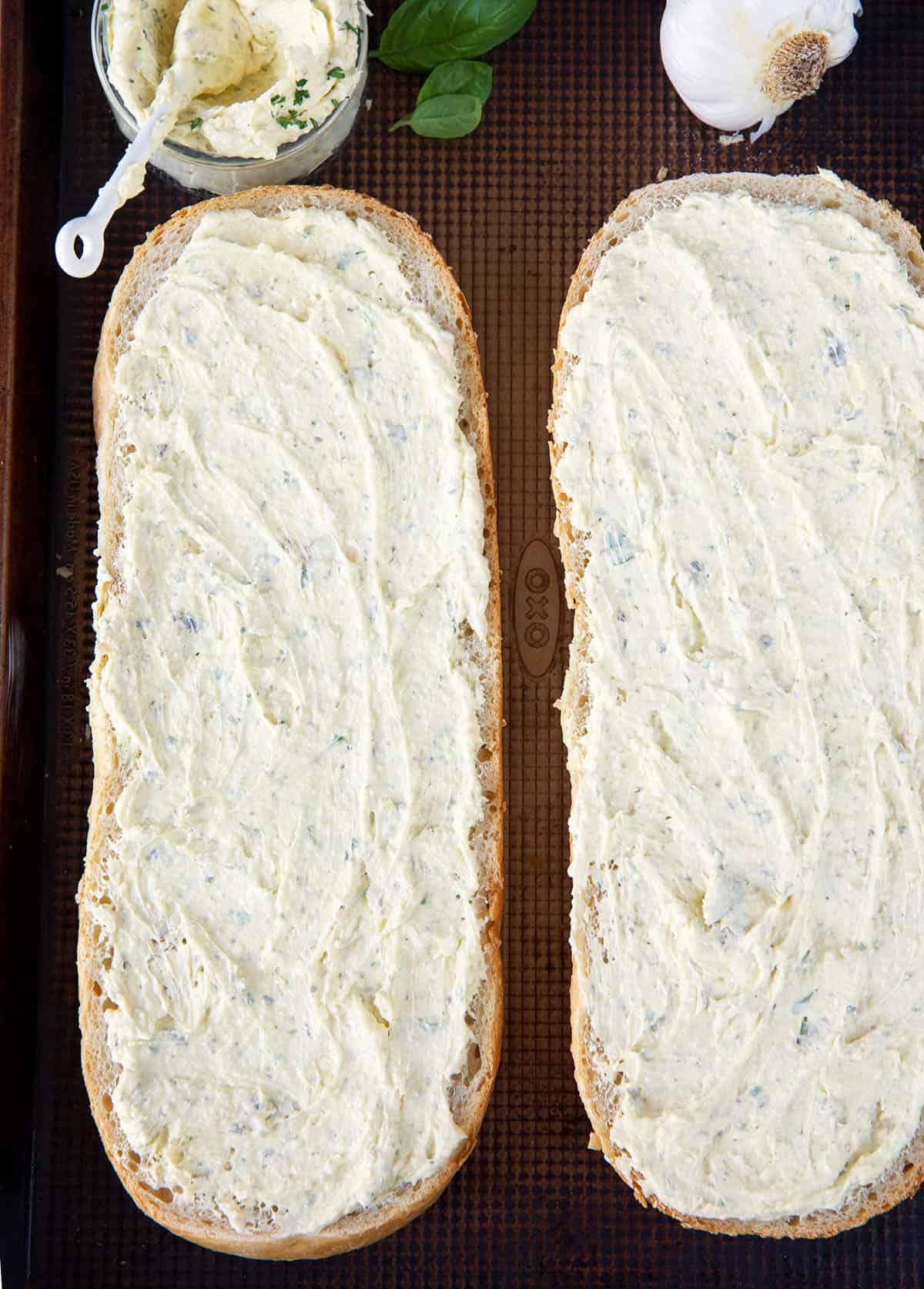 Pane all'aglio fatto in casa 3 Due metà di una baguette sono spalmate con la crema di burro all'aglio.