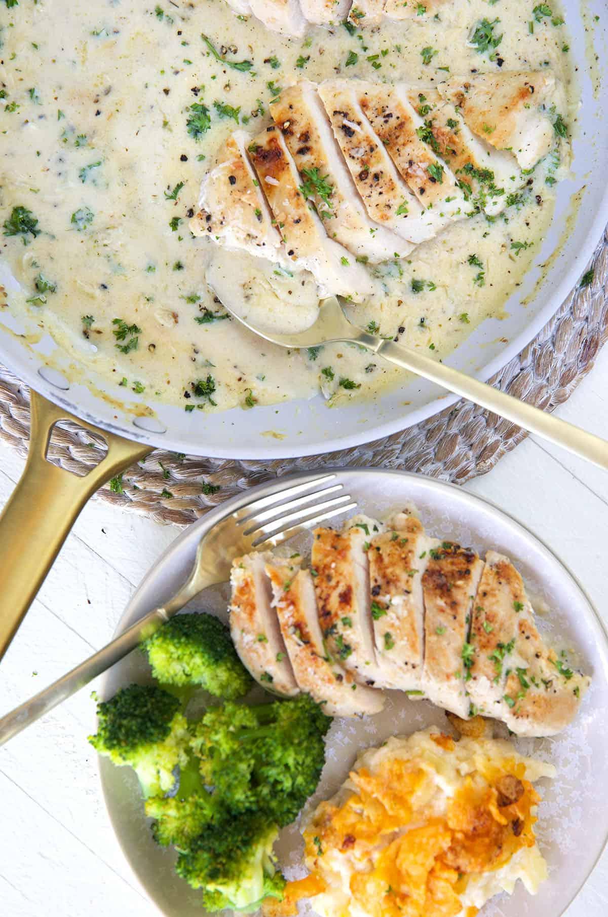 **Petto di Pollo Scottato in Padella con Salsa al Parmigiano e Aglio** 3 Un cucchiaio è posizionato in una padella piena accanto a un piatto con pollo e contorni.