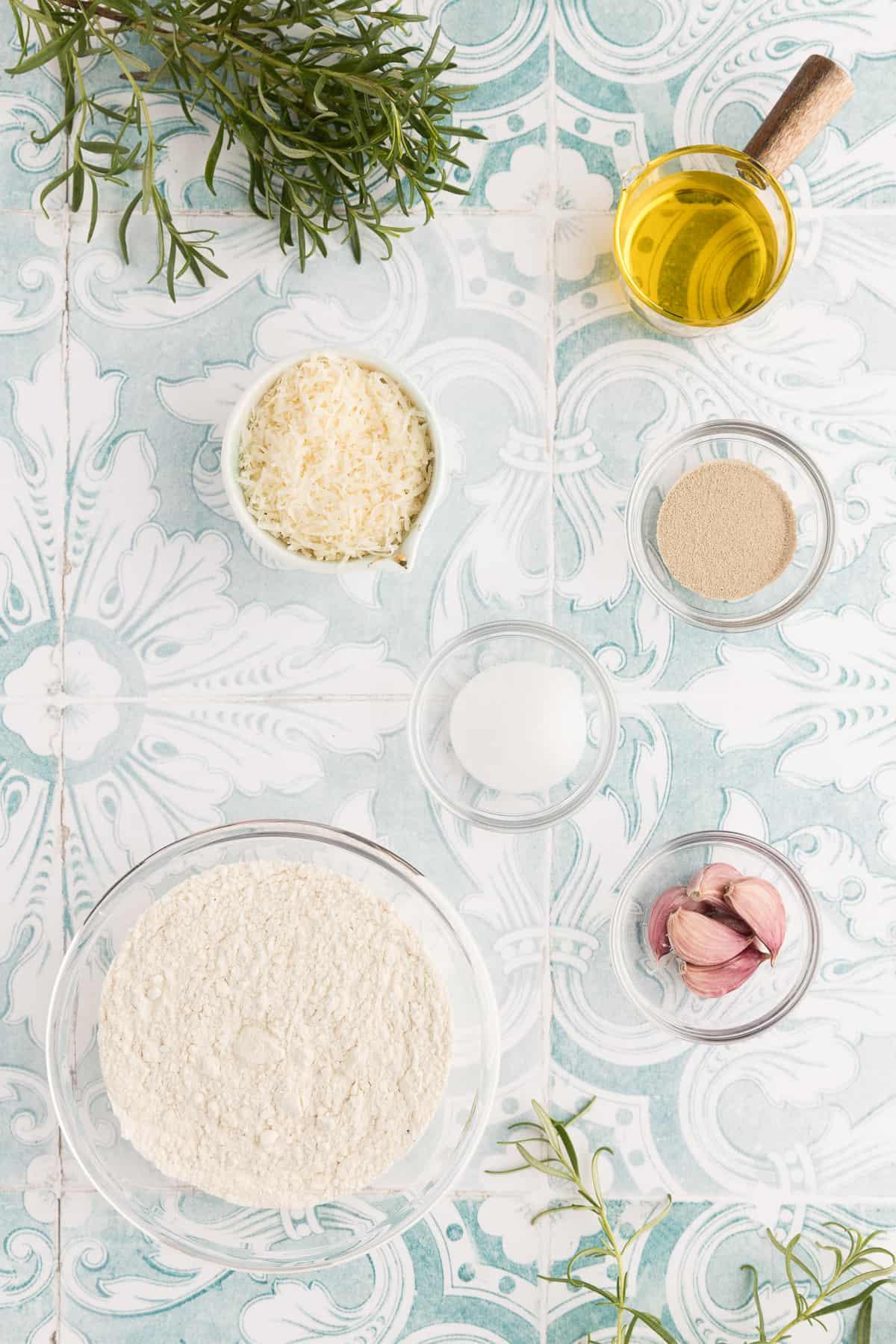 Focaccia all'Aglio e Rosmarino 3 Gli ingredienti per la focaccia sono posizionati su una superficie blu e bianca.