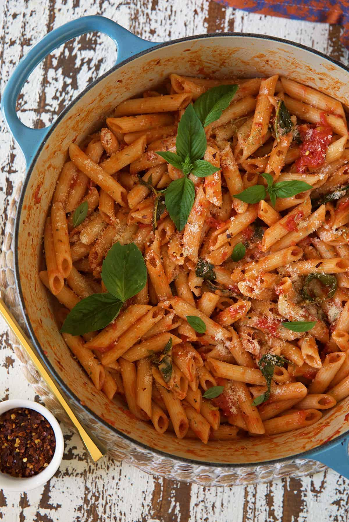 Penne al Pomodoro Veloce e Semplice 3 Una pentola in ghisa bianca e blu piena di penne al pomodoro cotte, guarnite con basilico fresco.