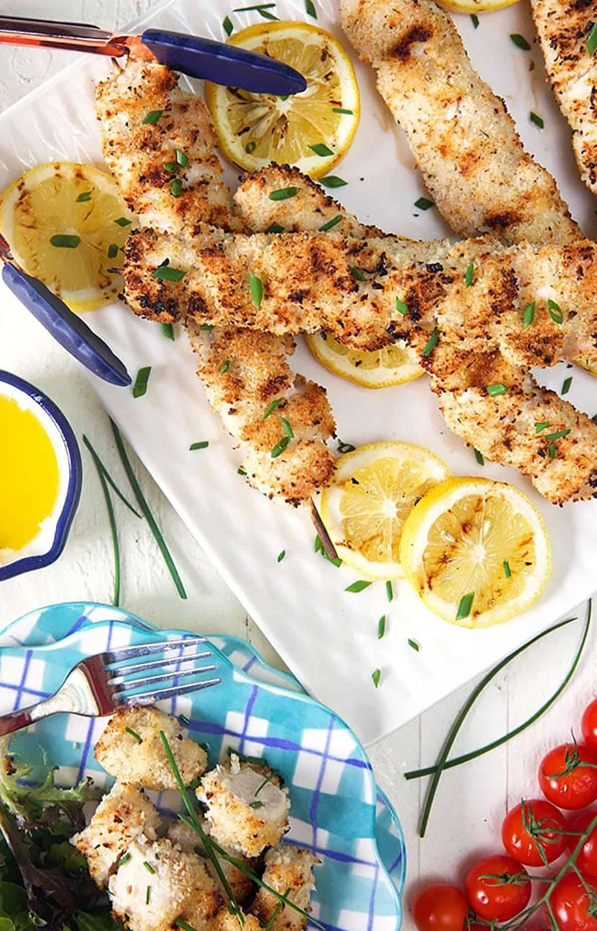 Spiedini di Pollo alla Griglia 4 Spiedini di pollo spiedini su un piatto bianco con fette di limone e un mucchio di pomodori ciliegino.
