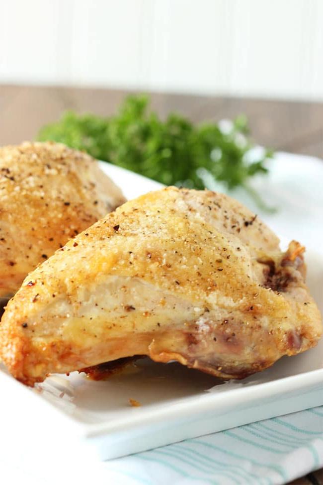 Le migliori ricette di petto di pollo al forno 4 Petto di pollo arrosto al forno su un piatto bianco con prezzemolo sullo sfondo.