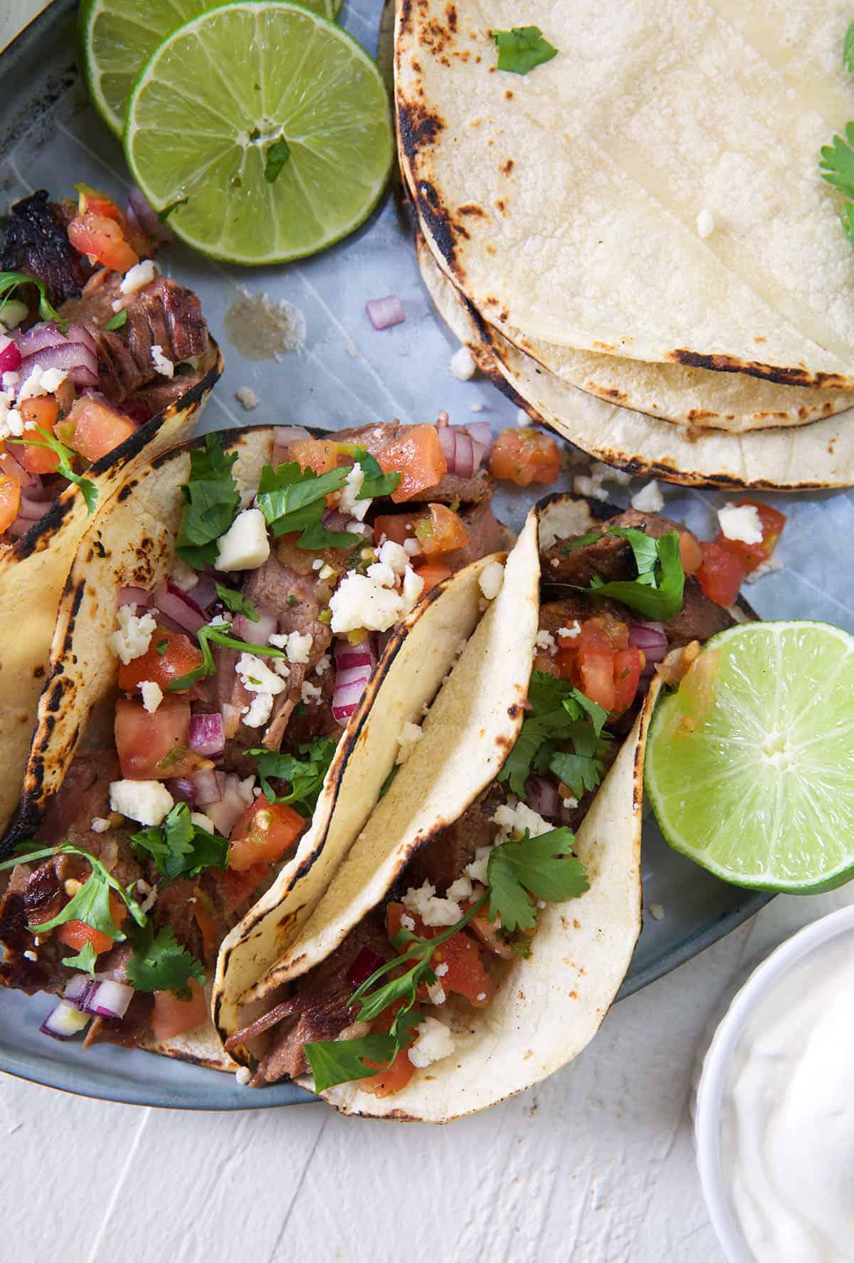 Semplici Tacos di Carne Asada 4 Lime dimezzati e tortillas extra sono posizionati accanto ai tacos su un piatto.