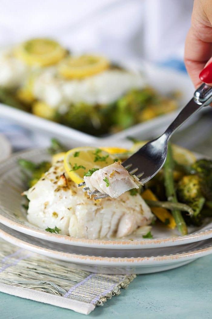 Merluzzo al Forno al Limone e Verdure 4 Una forchetta con un boccone di merluzzo al forno al limone su un piatto bianco con verdure verdi.