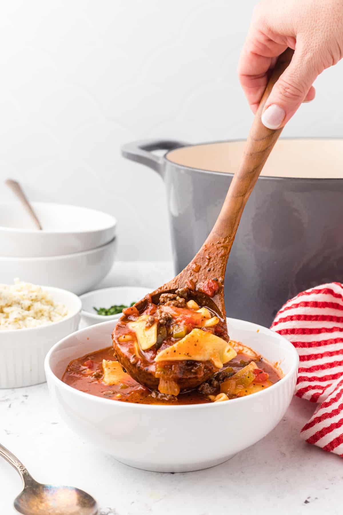 Zuppa di Lasagna Veloce e Facile 4 Un grande mestolo di legno sta versando la zuppa in una ciotola bianca.