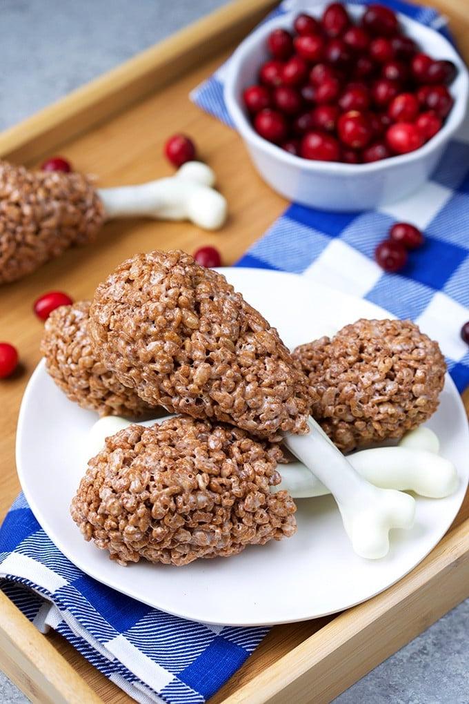 Cosce di tacchino di riso soffiato 4 Cosce di Tacchino di Rice Krispies su un piatto bianco con un tovagliolo a quadri blu e bianchi su un vassoio di legno.