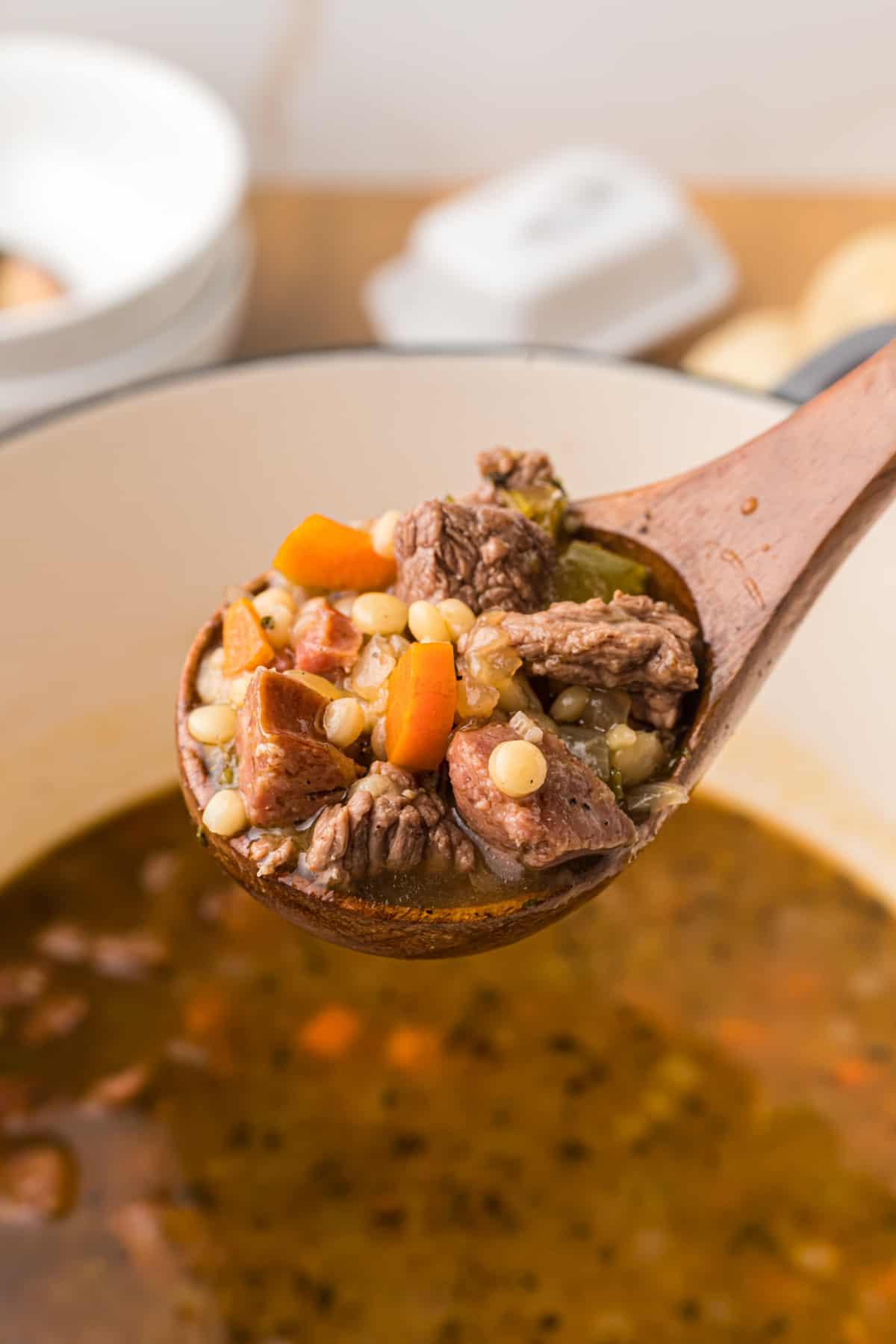 Zuppa di Manzo e Orzo con Salsiccia Andouille 4 Un cucchiaio di legno ha sollevato una piccola porzione di zuppa dalla pentola.