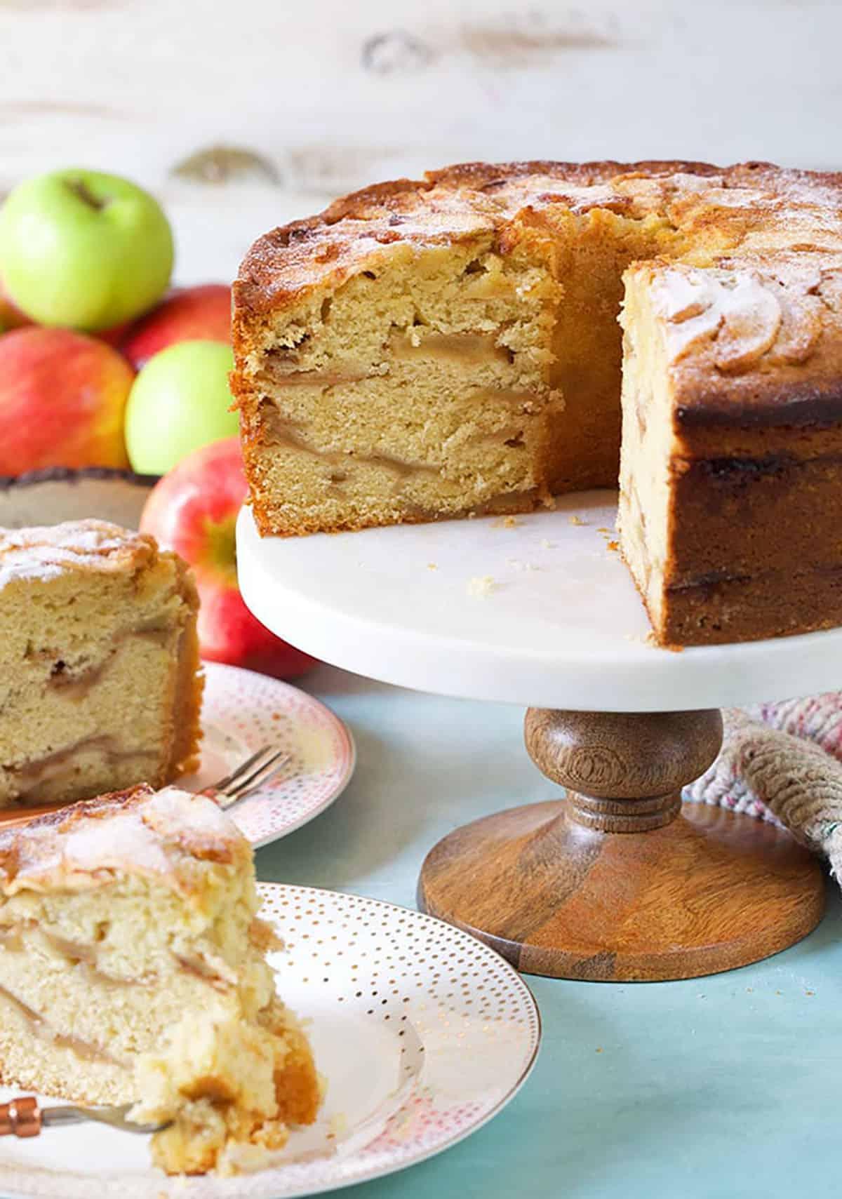 Torta di Mele Ebraica 4 Torta di mele ebraica con due fette tagliate e mele sullo sfondo.
