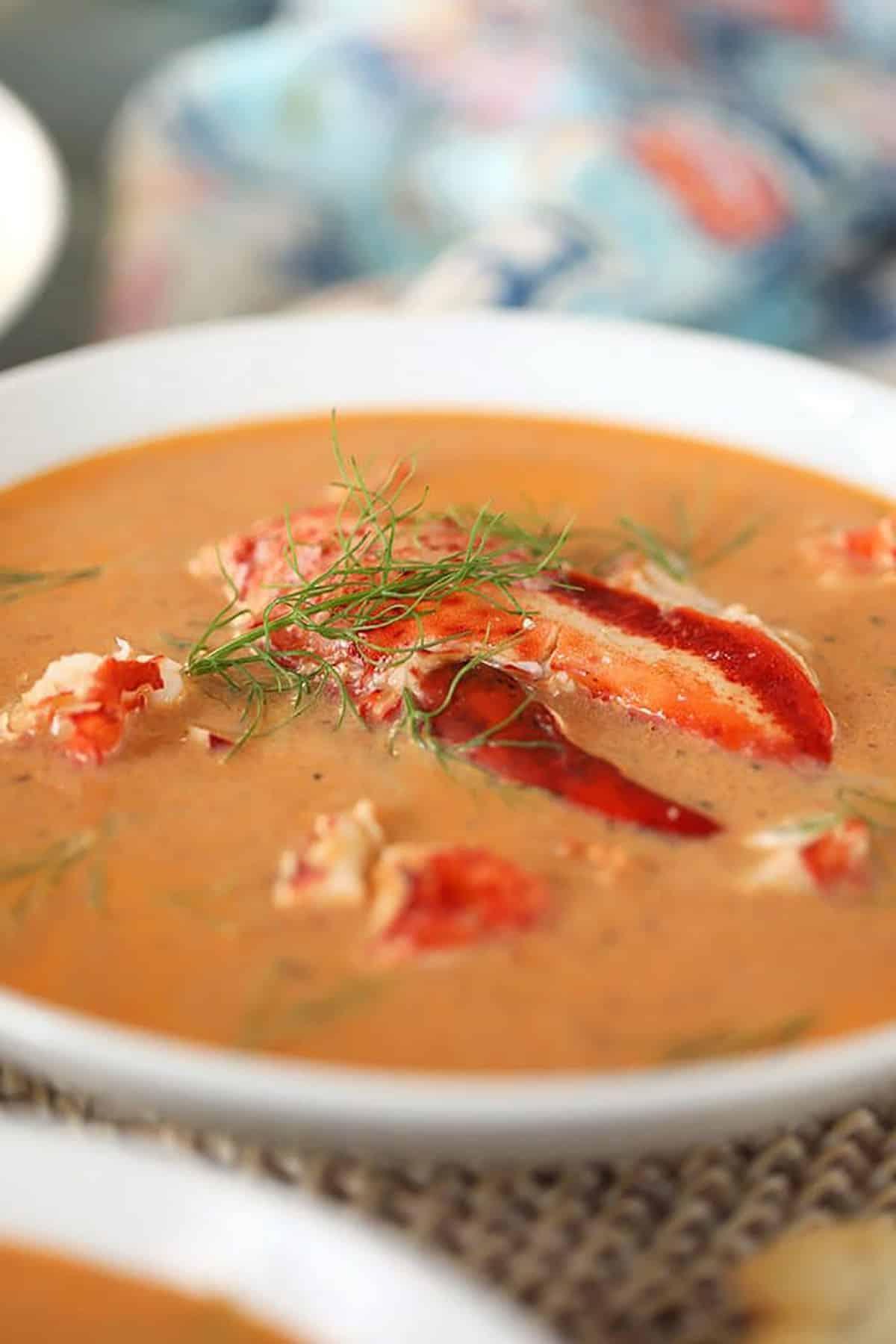 Bisque di Aragosta Facile 4 Primo piano di bisque di astice in una ciotola bianca con una chela di astice al centro della ciotola.