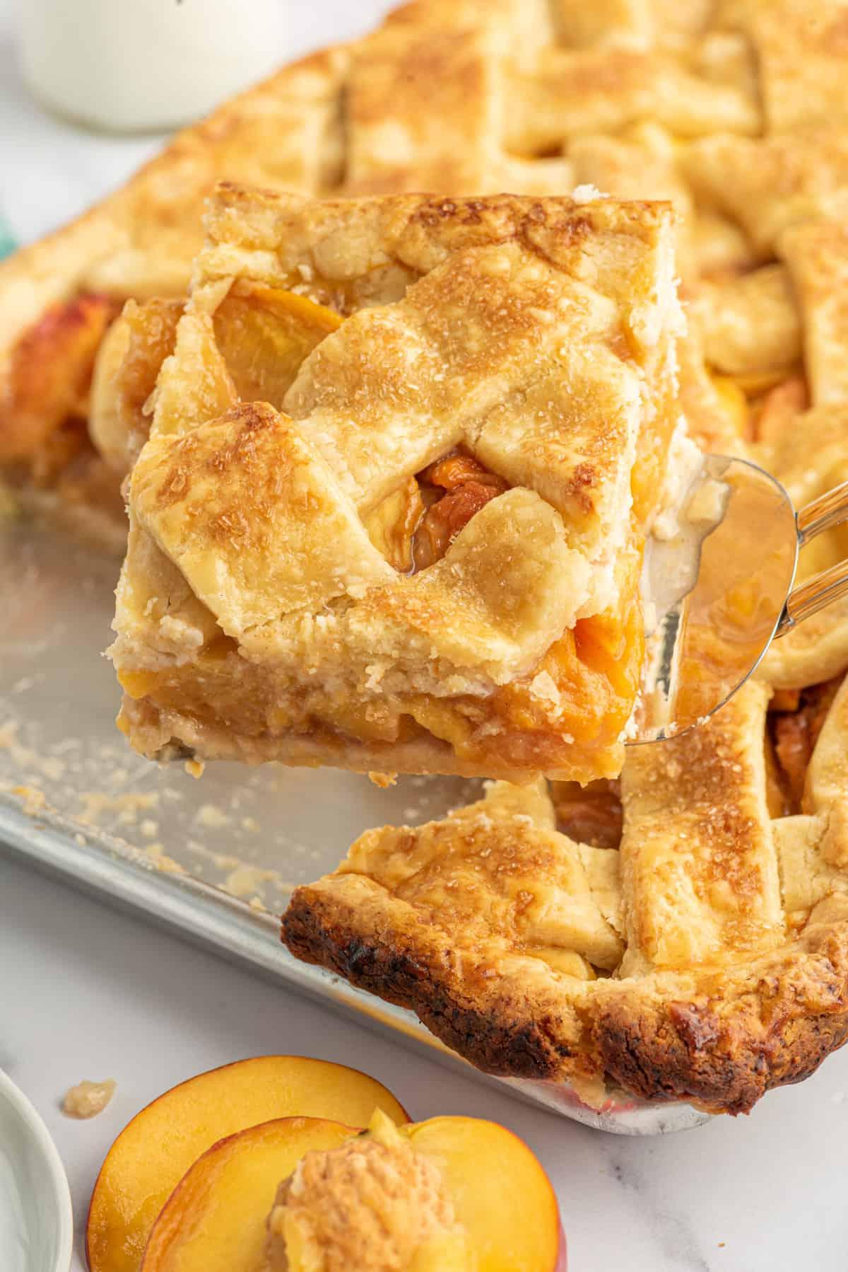 Facile Torta Classica di Pesche in Teglia 4 Una fetta di torta di pesche su teglia viene sollevata dalla teglia.
