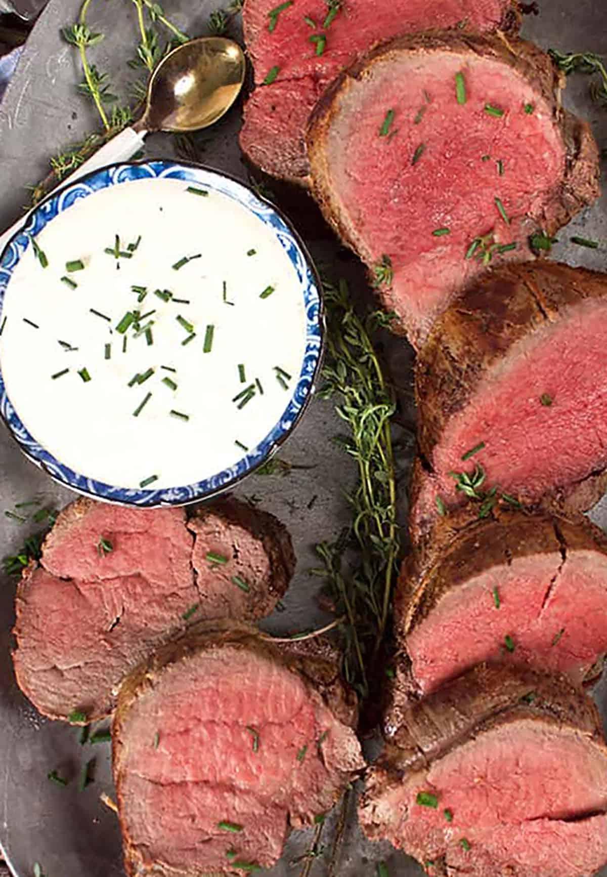 Arrosto Semplice di Filetto di Manzo 4 Piatto con filetto di manzo affettato e una ciotola di salsa al rafano.