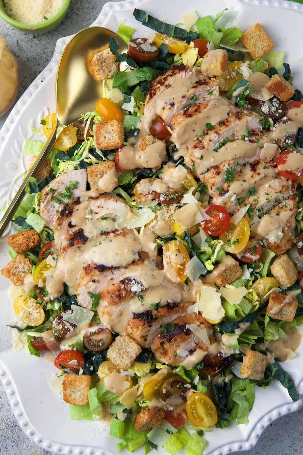 Insalata Caesar con Pollo 5 Un grande cucchiaio da portata è posizionato su un piatto bianco con insalata.