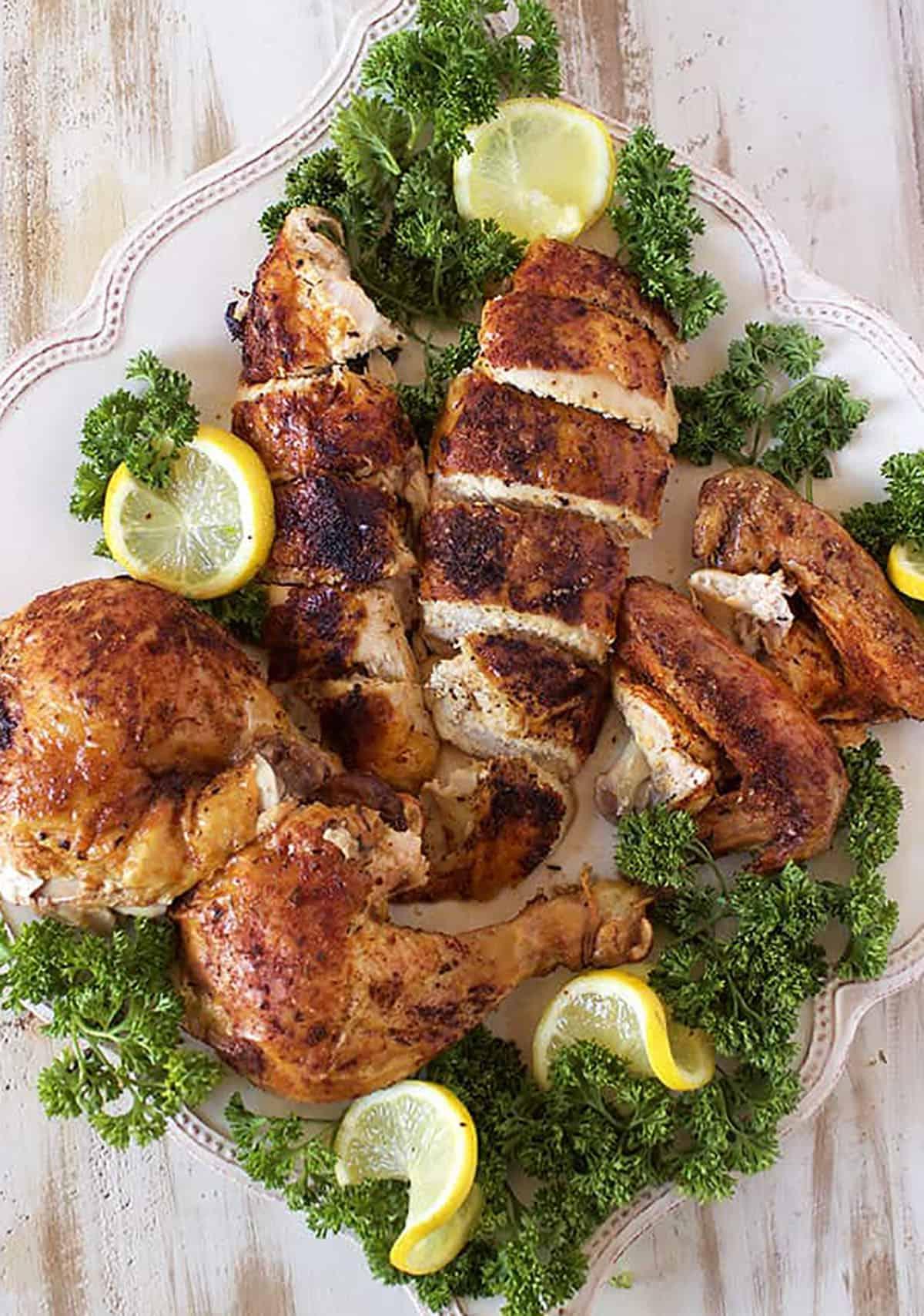 Come preparare il Pollo allo Spiedo 5 Pollo Arrosto intagliato e disposto su un piatto quadrato con rametti di prezzemolo e fette di limone.