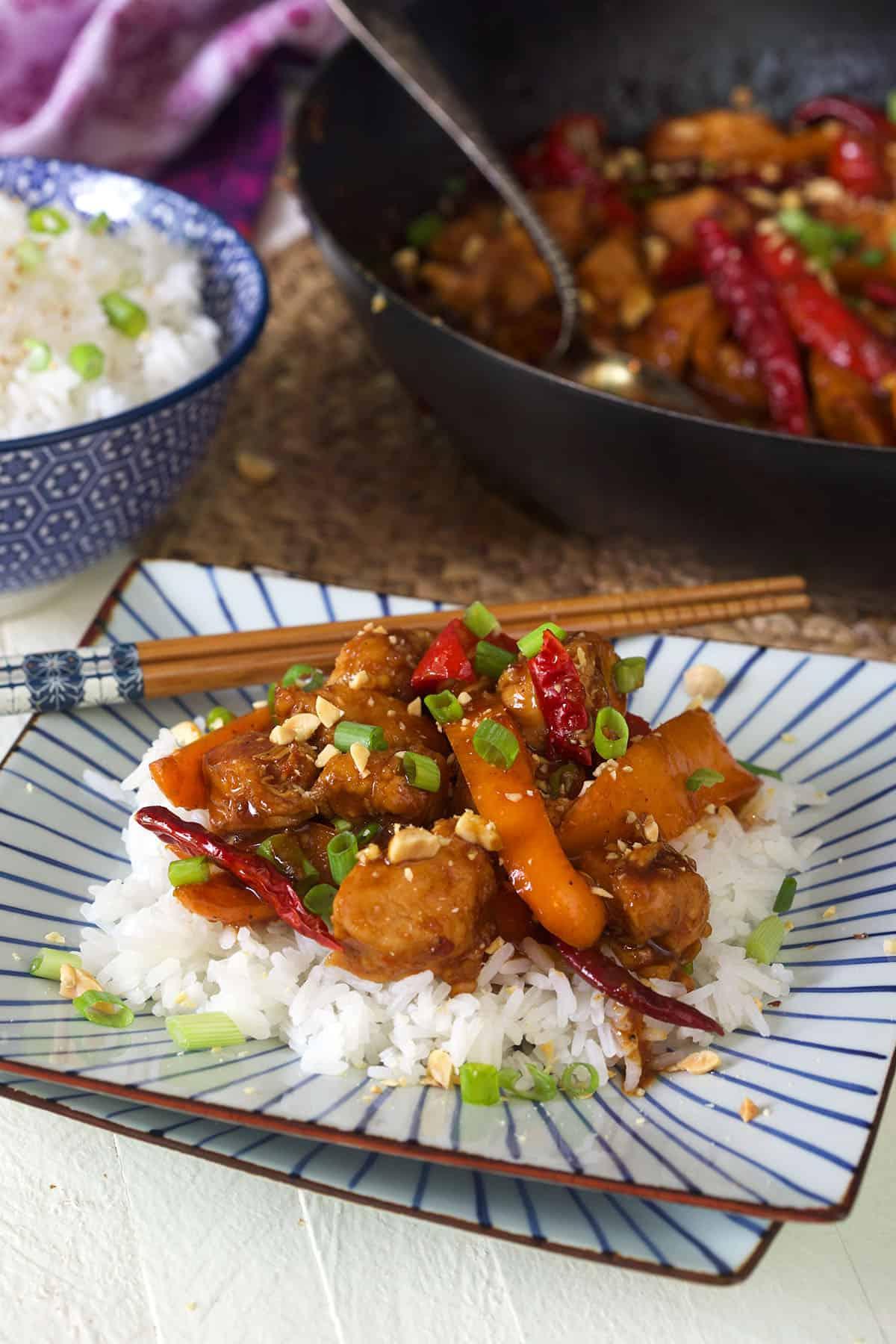 Pollo Kung Pao Facile 5 Un piatto a strisce blu e bianche contiene una porzione di pollo e riso.