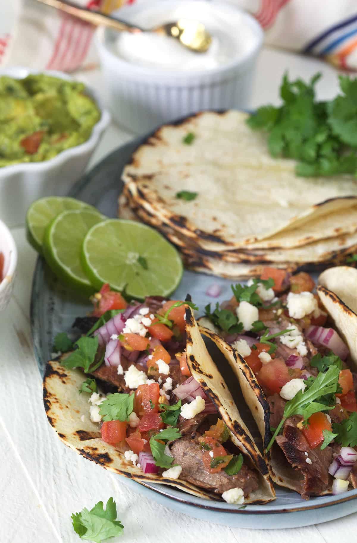 Semplici Tacos di Carne Asada 5 Tortillas, lime e tacos sono tutti impiattati insieme.
