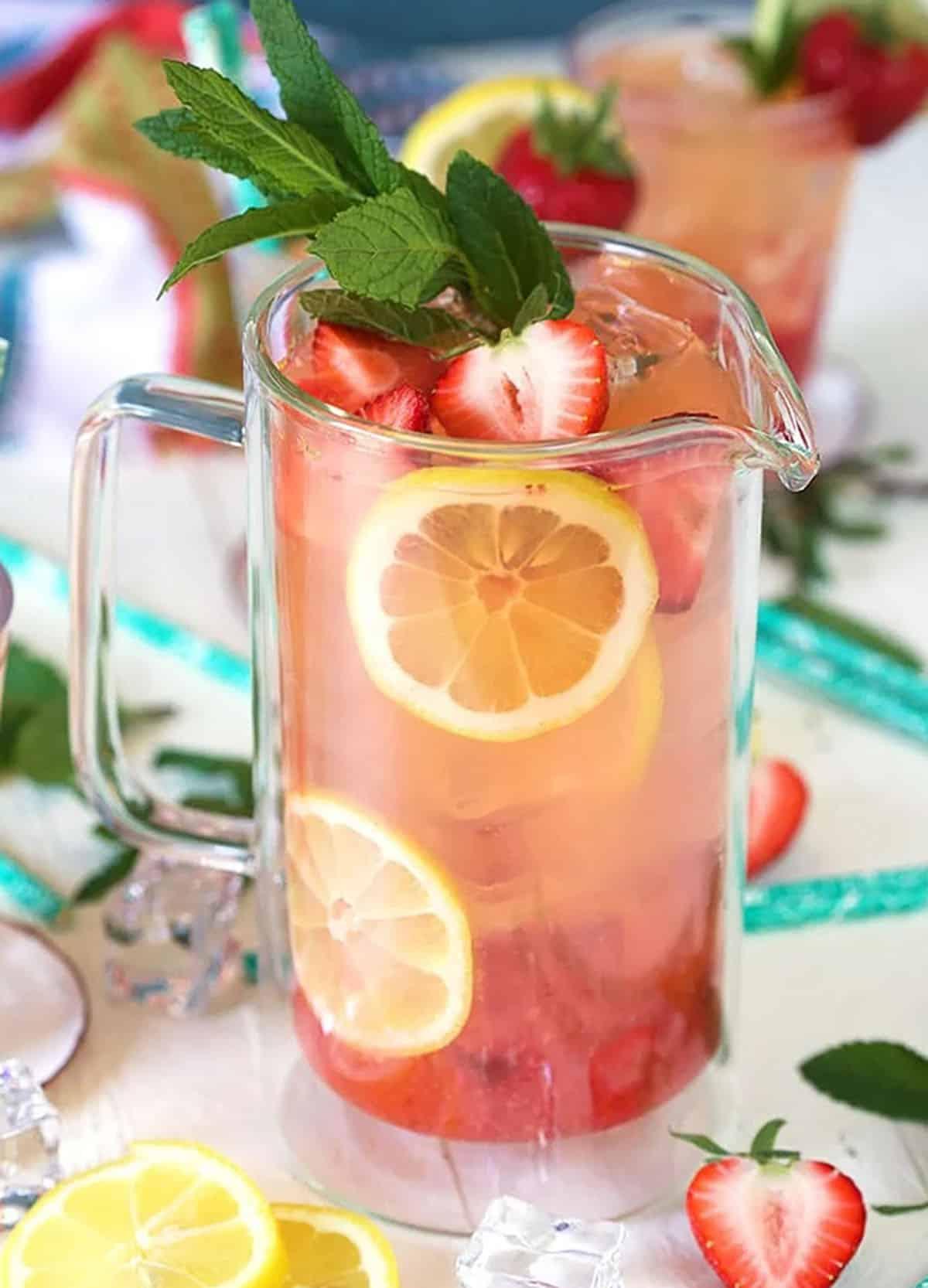 Limonata alle Fragole Fatta in Casa 5 Limonata alla fragola in una brocca di vetro con limoni e fragole disposti nella brocca come guarnizione.