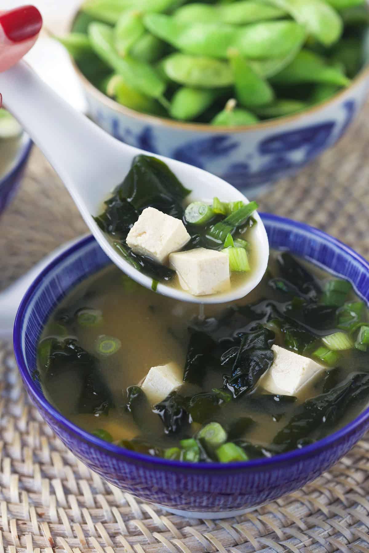 Zuppa di Miso Veloce e Facile 5 Un cucchiaio bianco solleva una porzione di zuppa dalla ciotola, con il vapore che sale delicatamente.