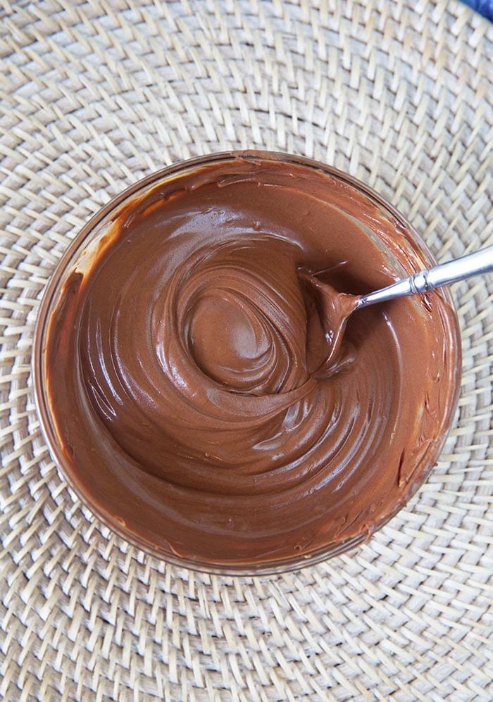 Biscotti Pagliaio Senza Cottura 5 Cioccolato fuso in una ciotola di vetro con un cucchiaio.