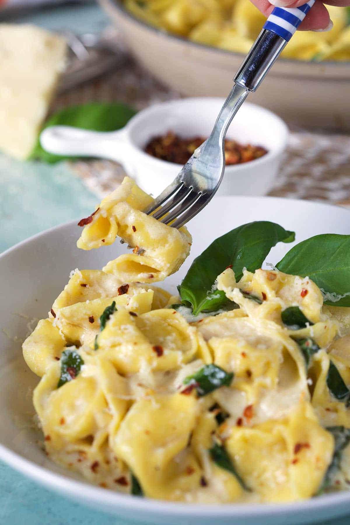 Tortellini all'Asiago 5 Una forchetta solleva un pezzo di tortellino cremoso dal piatto, mostrando la sua consistenza invitante.