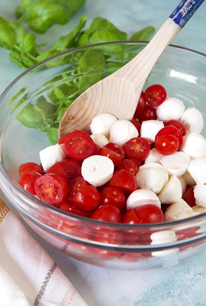Insalata di Pomodoro e Mozzarella 5 Pomodori e mozzarella mescolati in una ciotola di vetro con un cucchiaio di legno, per distribuire il condimento.
